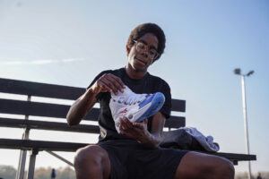 A boy sitting on a bench holding a pair of Reebok Questions