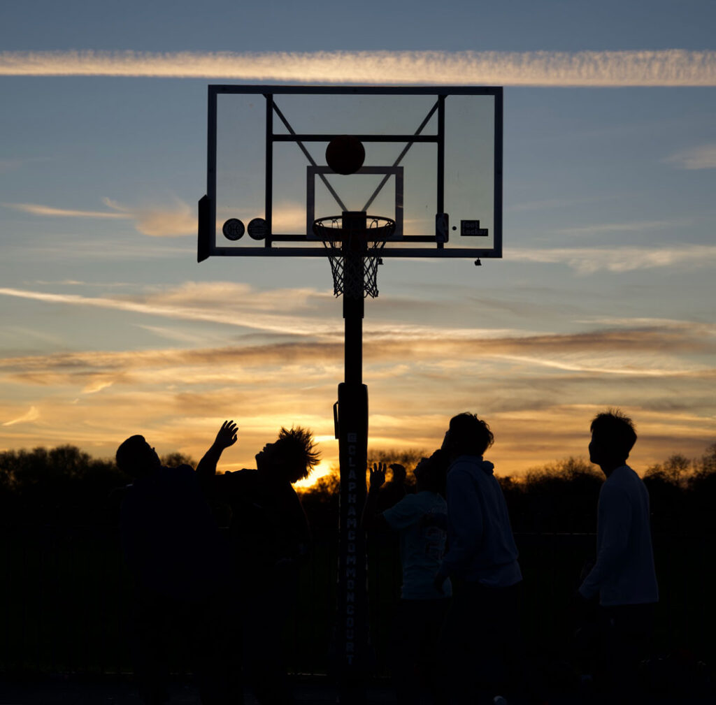 An outdoor basketball scrimmage, with a sunset in the background